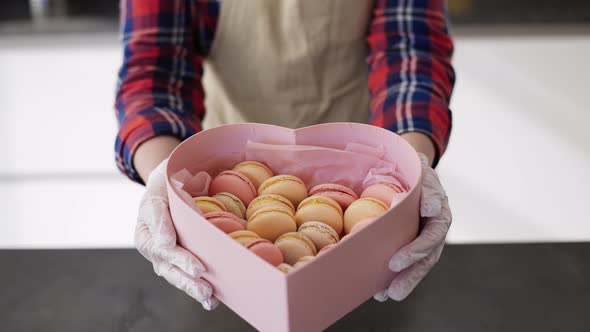 Confectioner in Apron Holding Box with Macaroons Cookies at the Kitchen