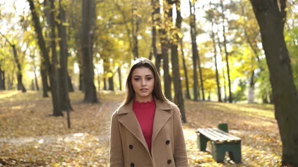 Brunette Stands in Sunny Autumn Park Admires the Nature and Looks at Camera