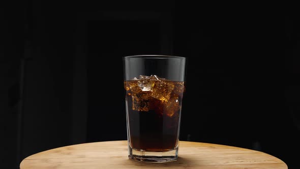 A glass with a dark, sweet drink and ice cubes stands on the kitchen board