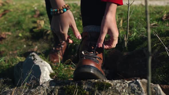 Young Caucasian Traveling Woman with Backpack Tying Up Shoe Laces on Her Boots on a Pathway in