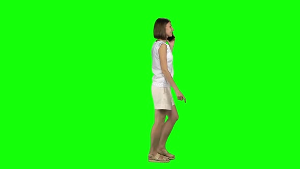 Woman with Brown Smooth Haircut Is Calmly Walking, Talking on Mobile Phone at Green Screen. Profile