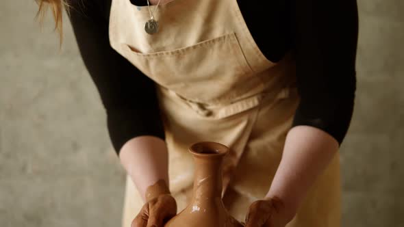 Cheerful Young Goodlooking Woman Wearing Apron Sitting in Pottery and Making Clay Jug on Potter