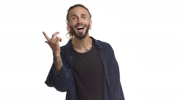 Attractive Bearded Male Model with Tattoos on Face and Body Cant Hear you Pointing at Ear and