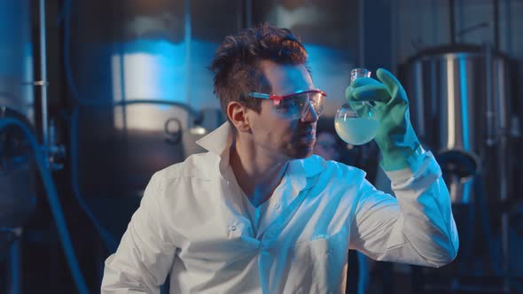 Mad Scientist Drinking Blue Liquid From Glass Flask in Industrial Lab