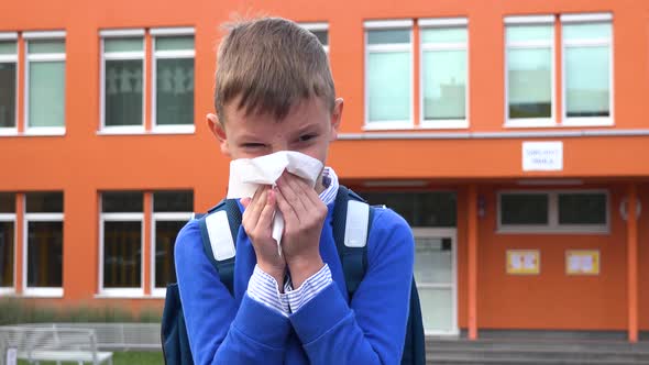 A Young Boy Blows His Nose in Front of an Elementary School in the Background