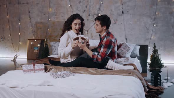 A Couple in Love in Winter Sweaters and Thick White Socks Are Sitting on the Bed