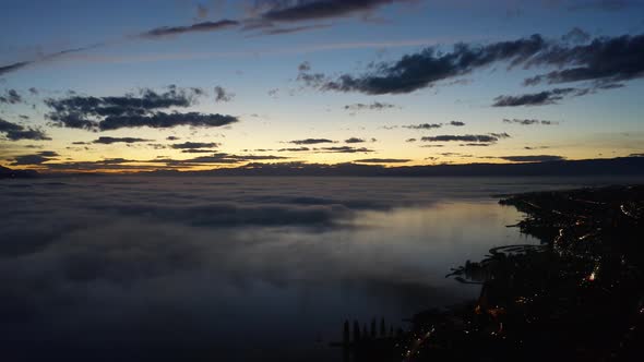 High aerial over shore of Lake Léman at sunset with patches of fog low over the lake reflecting in t