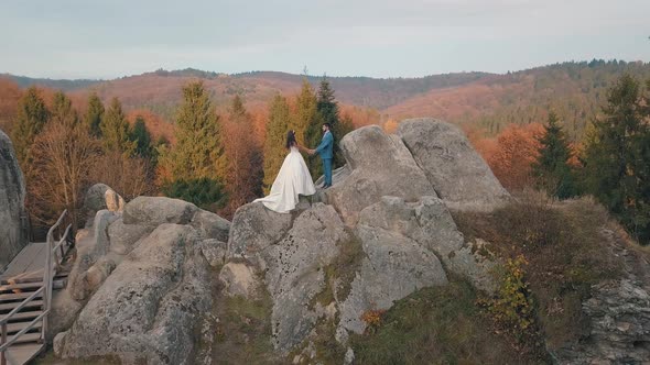 Newlyweds Stand on a High Slope of the Mountain. Groom and Bride. Arial View