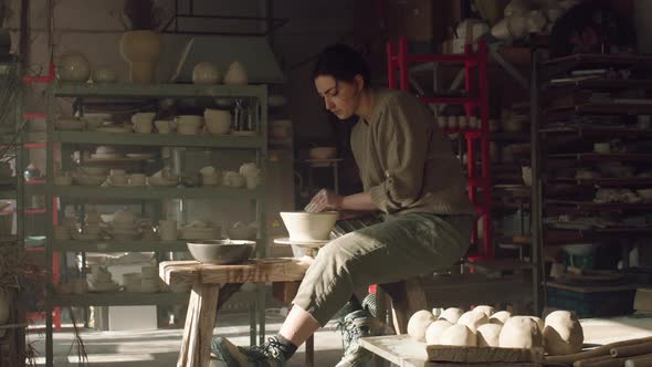Craftswoman Is Sitting On Potter's Wheel and Making Bowl