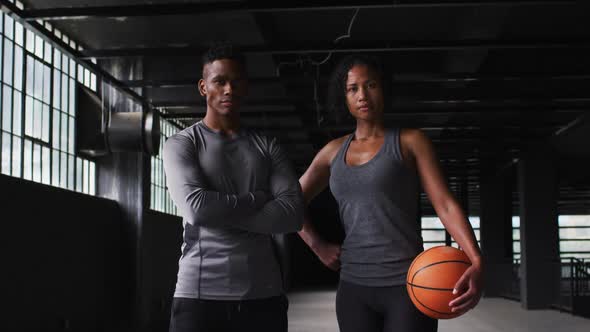 African american man and woman standing in an empty building holding a basketball