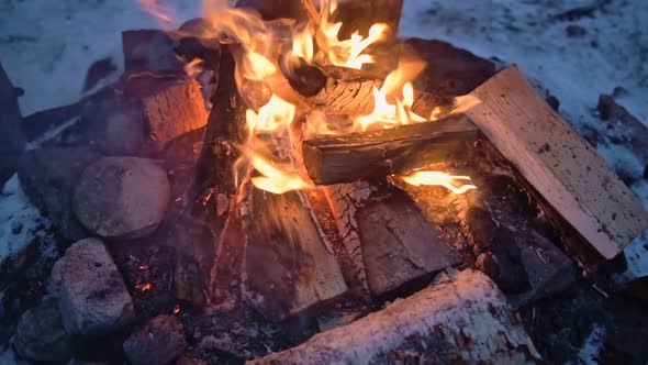 Logs burning in a outdoor campfire, surrounded by snow, on a windy evening in Lapland, Finland