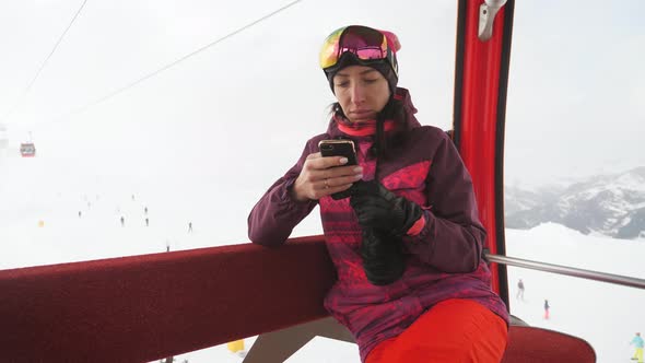 Attractive Young Woman at a Mountain Ski Resort. Standing on a Snow Using on Her Mobile Phone