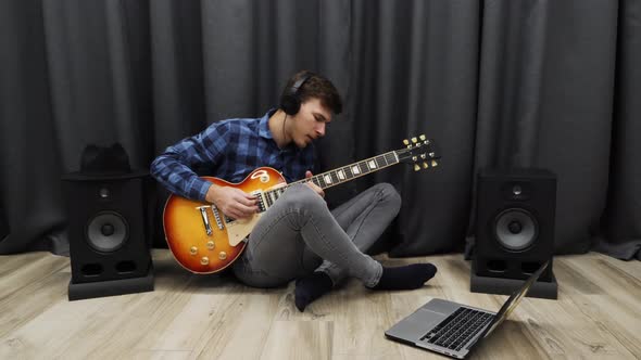 Man playing on electric guitar wearing headphones practicing song in home music recording studio