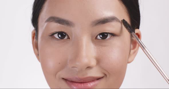 Young Asian Woman Brushing Her Eyebrows with Mascara Close Up Studio Portrait Slow Motion