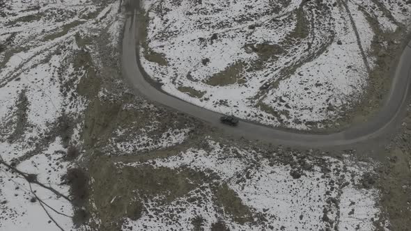 Aerial Birds Eye View Of Black SUV Driving Winding Snow Rocky Mountain Roads In Winter Through Hunza