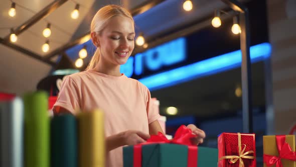 Lowangle View of Young Cheerful Woman Seller Wrapping Christmas Gift Box Tying Red Ribbon and