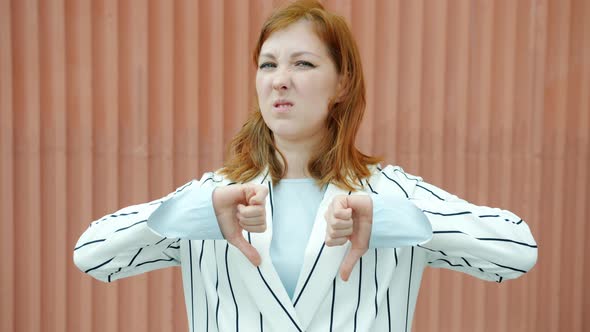 Slow Motion Portrait of Disgusted Redhead Lady Showing Thumbsdown Hand Gesture and Wrinkling Nose