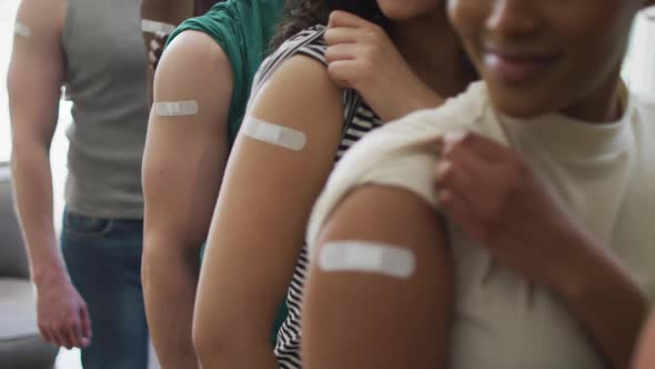 Mid section of group of diverse young people showing their vaccinated shoulders at home