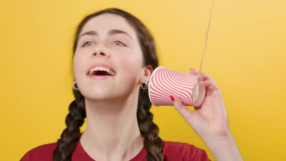 A smiling woman communicates on a toy walkie-talkie made out of a paper cup.