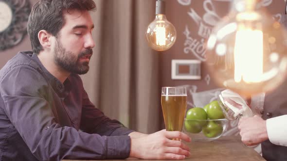 Man Sips a Bit of Beer While at a Bar Counter Talking To the Bartender