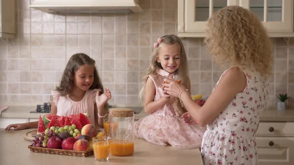 Beautiful Girl Sitting on Countertop Drinking Healthful Juice Enjoying Weekend with Mother and