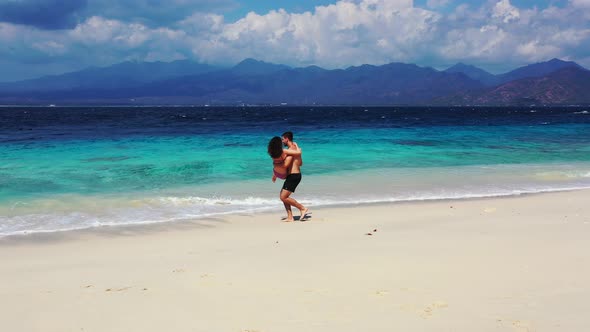 A young Caucasian man carrying and spinning his partner around in the shallow water of a tropical is