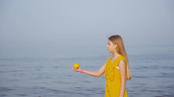 Young Girl Throws a Lemon in Front of the Sea