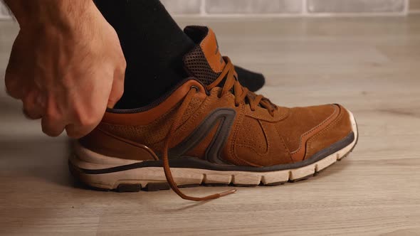 A Closeup of a Man's Black Socked Foot Putting on a Brown Leather Walking Sneaker