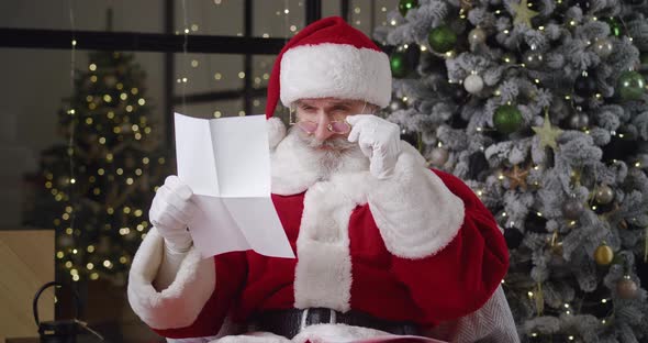 Santa Claus in Christmas Costume Sitting in Armchair Against Christmas Tree at His Residence