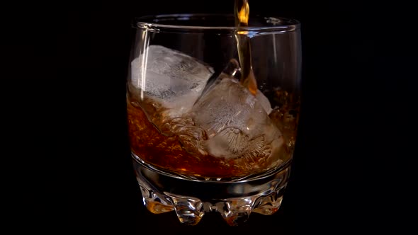 Pouring whiskey into a glass with ice on an isolated black background. Slow motion.