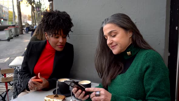 Cheerful black woman looking on smartphone with ethnic friend