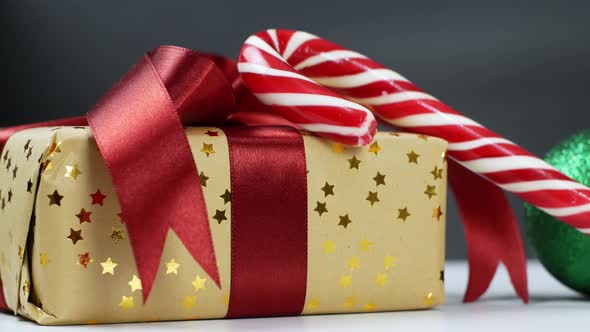 A Christmas gift arrangement with a red bow, Christmas tree balls, and a caramel cane.