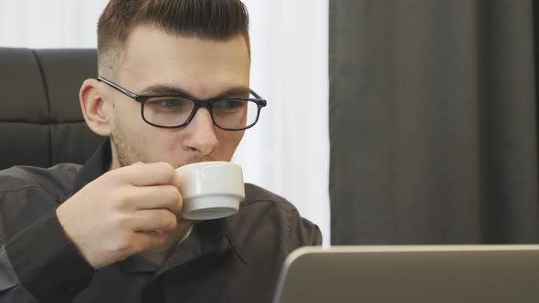 Portrait of man drinking coffee sitting at his modern office desk and laptop