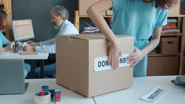 Closeup of Charity Company Activist Preparing Cardboard Boxes for Donation in Office