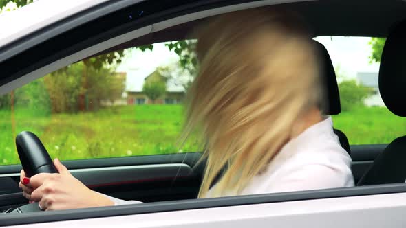 Young Attractive Blond Woman Sits in the Car, Listens Music and Dances Crazy