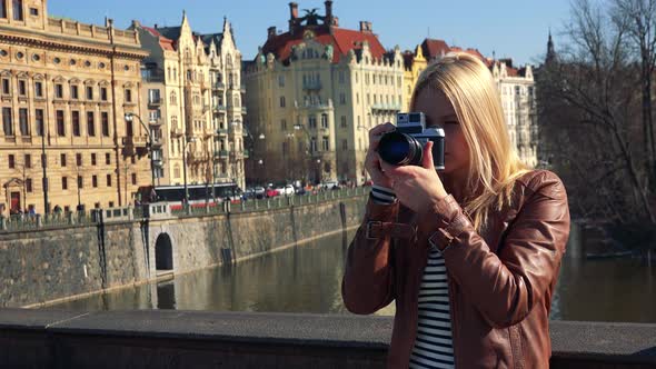 A Young Attractive Woman Takes Photos of Something Off the Camera - River and Buildings in a Street