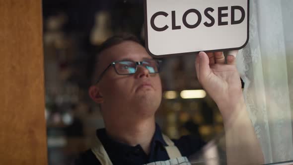 Caucasian waitress changing sign on doors from open to closed. Shot with RED helium camera in 8K.