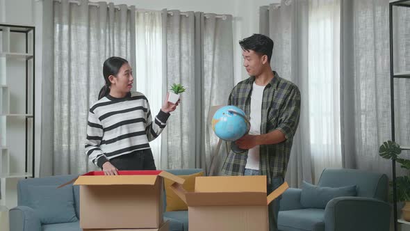 Asian Couple Moving Into A New House Unpacking The Cardboard Boxes And Taking Stuff Out Of Them