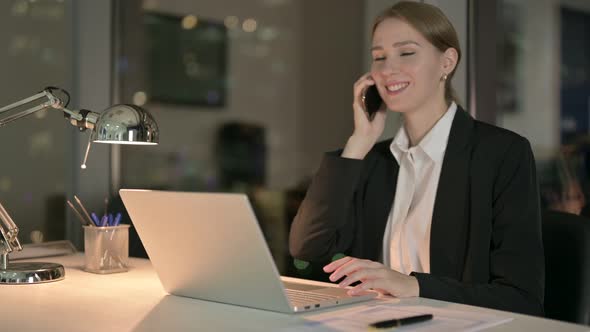 Cheerful Businesswoman Talking on Smartphone in Office at Night