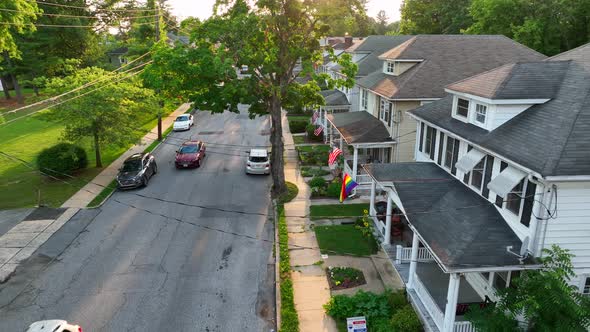 Establishing shot of cars driving on small town street. Pride flags and American flags visible hangi