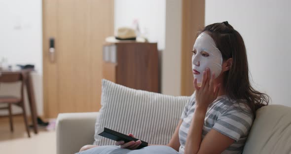 Woman apply facial mask and watch tv at home