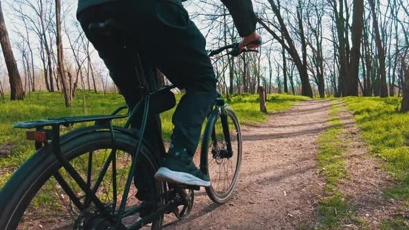 Young Guy Rides a Bicycle Along a Path in a Green Forest Rear View in Slow Mo