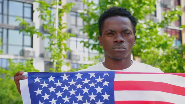 Close Up Afroamerican Man Holding an American Flag and Looks Camera