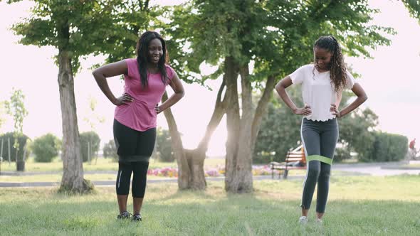 Two African Women Exercising with Rubber Band at Dawn in Public Park