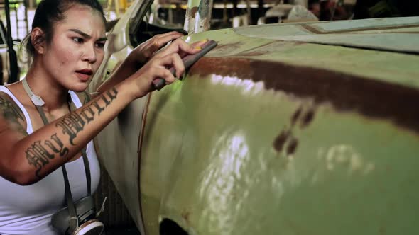 Attractive young woman mechanical worker repairing a vintage car in old garage.