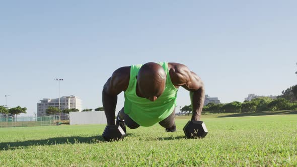 Fit african american man exercising outdoors doing press ups holding dumbbells