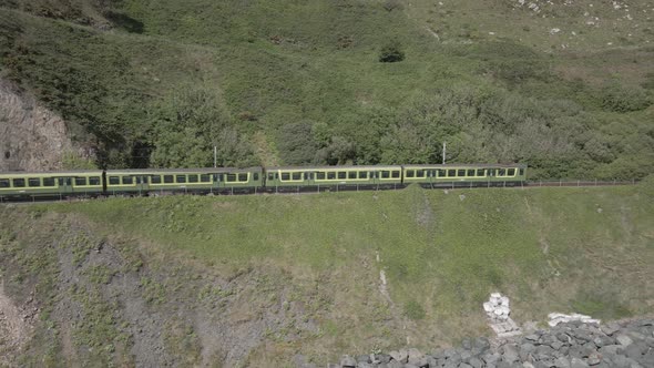 Train Exiting Tunnel In Bray Head Mountain In County Wicklow, Ireland On A Sunny Day. tracking shot