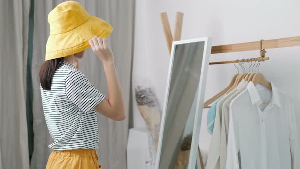 Lovely Asian girl trying the new hat in front of the mirror.