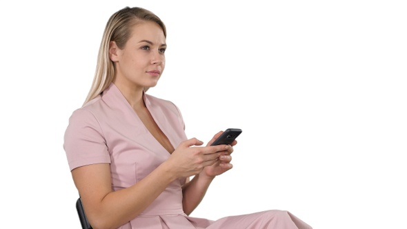 Smiling Blonde Woman Sitting and Using Smartphone on White