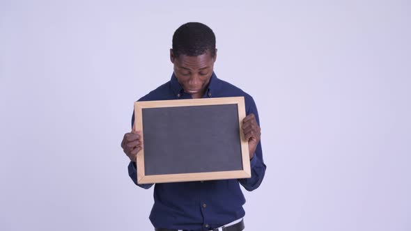 Young Happy African Businessman Holding Blackboard and Looking Surprised